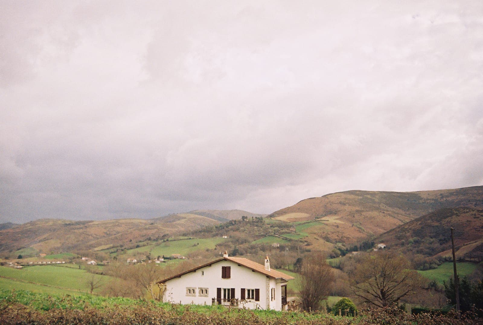 white farmhouse in green hills under a heavy sky