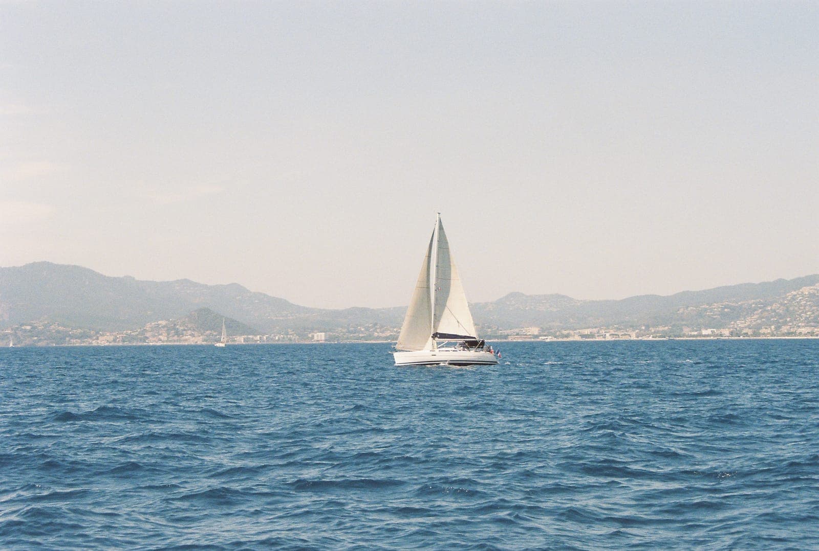 sailboat crossing blue water with the coast behind