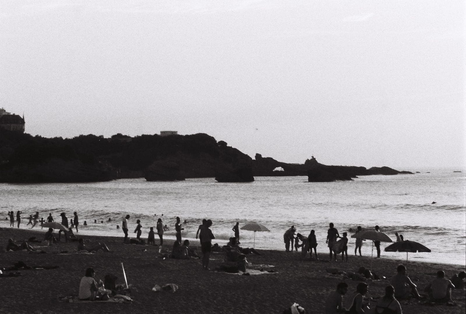crowded beach below a rocky point, in black and white