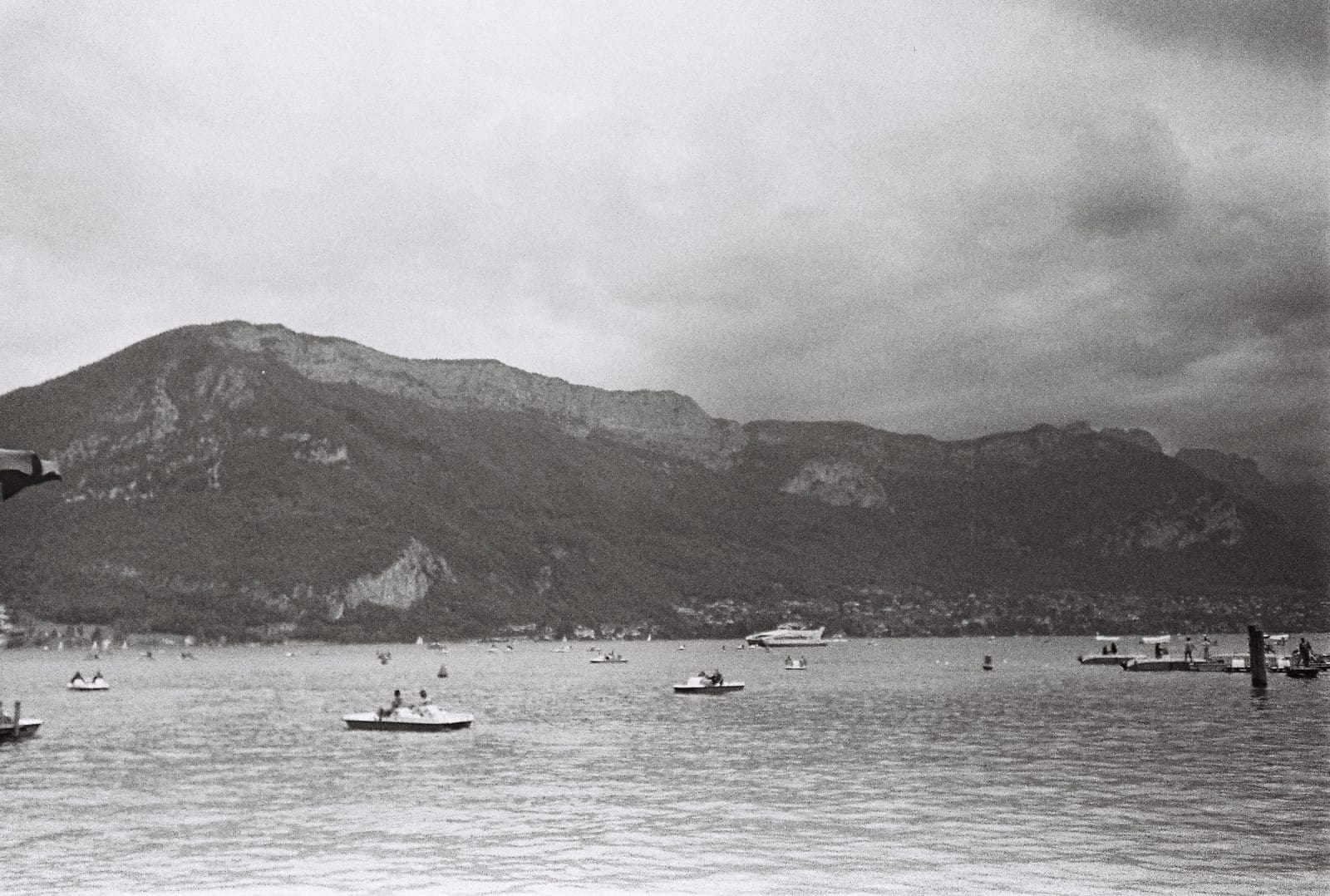 boats on a lake beneath mountains, in black and white