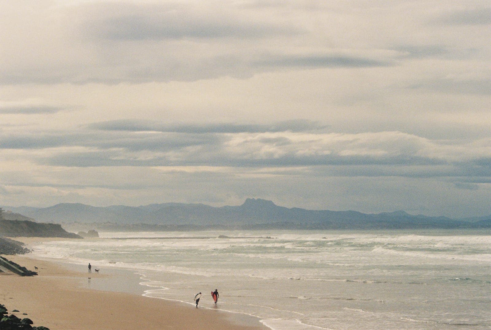 beach at golden hour with walkers by the water and mountains beyond