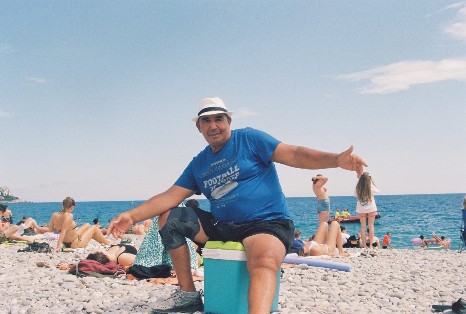 man in a blue t-shirt and white hat sitting on a pebble beach